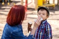 Mother wipes face of her toddler son. The boy is holding an ice-cream in waffle cone in hand. Mother care concept Royalty Free Stock Photo