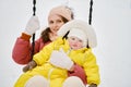 A mother woman with a toddler baby rides on a swing in a snowy park.t Royalty Free Stock Photo