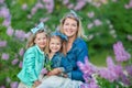 Mother woman with two cute smiling girls sisters lovely together on a lilac field bush all wearing stylish dresses and Royalty Free Stock Photo