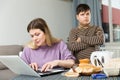 Mother working at laptop and unhappy preteen son standing near table