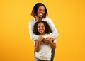 Mother& x27;s love. Happy loving african american mom cuddling her daughter from the back, standing over yellow background Royalty Free Stock Photo