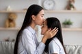 Mother& x27;s love. Loving asian mom kissing her daughter in forehead while spending time together at home, side view Royalty Free Stock Photo