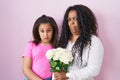 Mother and young daughter holding bouquet of white flowers in shock face, looking skeptical and sarcastic, surprised with open Royalty Free Stock Photo