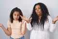 Mother and young daughter standing over white background clueless and confused expression with arms and hands raised Royalty Free Stock Photo