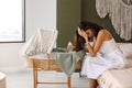 Young tired depressed mother holding milk bottle sitting near bassinet with newborn baby at home