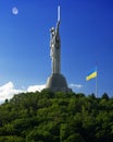 Motherland monument and waving ukrainian flag on green hill against blue sky in Kyiv, Ukraine Royalty Free Stock Photo