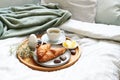 Mothers day breakfast served with love on bed. Coffee, croissant, egg and chocolate hearts on a wooden tray. Natural bed cloth.