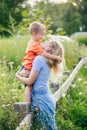 Mothers Day holiday. Young Caucasian mother and boy toddler son hugging embracing in park outdoors on summer day. Mom and child