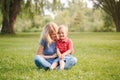 Mothers Day holiday. Young smiling Caucasian mother and laughing boy toddler son sitting on grass in park. Family mom and child Royalty Free Stock Photo