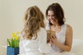 Mothers Day. The little daughter keeps a gift and flowers for her mother. Background interior of bedroom, mother in bed, morning Royalty Free Stock Photo