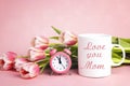 Mothers day message on white coffee mug with tulip flowers and alarm clock on pink background