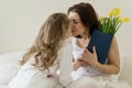Mothers Day. Mother holds a bouquet of flowers kisses and hugs a little daughter. Background interior of bedroom, mother in bed, m