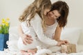 Mothers Day. The mother is hugging her little daughter. Background interior of bedroom, bouquet of flowers, gift, mom and child in