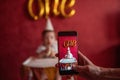 Mothers hand takes pictures of son on smartphone. Boy of one year in party hat holding birthday cake Royalty Free Stock Photo