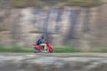 Motion blur image of a rider wearing helmet for safety, riding uphill on a red moped.