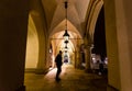 Motion blur of man walking through the columns at sukiennice Cloth Hall at night, with lamp lighting overhead. Krakow, Poland.