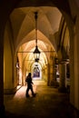 Motion blur of man walking through the columns at sukiennice Cloth Hall at night, with lamp lighting overhead. Krakow, Poland.