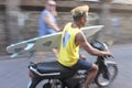 Motion blur of a young Indonesian man riding a scooter holding a surfboard in Kuta Bali Indonesia