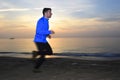 Motion blurred action of young sport man running outdoors on beach at sunset