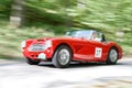 Motion blurred red color Austin Healey 3000 MKII classic car from 1961 driving in a country road Royalty Free Stock Photo