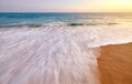 Motion blurred wave entering sandy beach at sunset