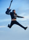 Motion and fun concept. Happy young man jumping in air and playing guitar over blue sky and clouds background Royalty Free Stock Photo