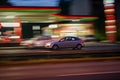 Motion shot of a gray car driving fast down a road near an illuminated gas station Royalty Free Stock Photo