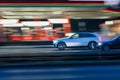 Motion shot of a white car driving fast down a road near an illuminated gas station Royalty Free Stock Photo