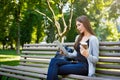 Motivated asian freelancer in the park. Girlon a bench, drinking coffee and working with tablet