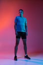 Portrat of Caucasian young sportive man in sportswear standing isolated on pink studio background with blue neon filter