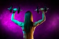 Motivated young woman fitness model exercise shoulders with professional dumbbells in neon lights in the studio. Back Royalty Free Stock Photo