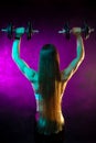 Motivated young woman fitness model exercise shoulders with professional dumbbells in neon lights in the studio. Back Royalty Free Stock Photo