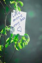 Motivating phrase love more worry less. On a green background on a branch is a white paper with a motivating phrase