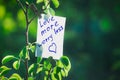 Motivating phrase love more worry less. On a green background on a branch is a white paper with a motivating phrase.