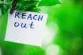 Motivating phrase reach out. On a green background on a branch is a white paper with a motivating phrase.