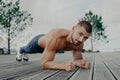 Motivational bearded man stands in plank pose, trains muscles and has strong body. Sporty adult guy performs push up exercise