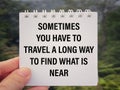 Motivational and inspirational wording. Sometimes You Have To Travel A Long Way To Find What Is Near written on white notepad.