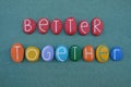 Better together, motivational slogan text composed with multi colored stone letters over green sand