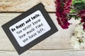 Motivational quote on chalkboard frame and white flowers on on wooden desk.