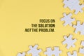 Motivational quote - Focus on the solution not the problem. With white jigsaw puzzle background on soft yellow background.