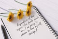 Motivational quote on note book with sunflowers on wooden desk.