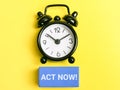 Selective focus phrase ACT NOW on wooden cubes with alarm clock over yellow background. Royalty Free Stock Photo