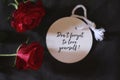 Motivational text message on white tag label paper - Do not forget to love yourself. With red roses on dark black background.