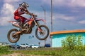 Motocross. The athlete on a motorcycle jumps high against the background of standing cars, blue sky and white clouds. Royalty Free Stock Photo