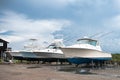 Motor boats stand on land under the open blue sky in the parking lot at the pier