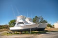 Motor boats stand on land under the open blue sky in the parking lot at the pier