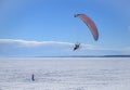 A motor paraplane flies over a frozen lake for a girl walking in the snow