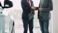 Motor showroom employee is giving car key to young male buyer and shaking hands, dealer is holding documents and Royalty Free Stock Photo