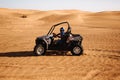 Male driver in helmet sit inside buggy quad car at desert sandy landscape