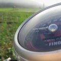 a motorbike speedometer with a green rice field background